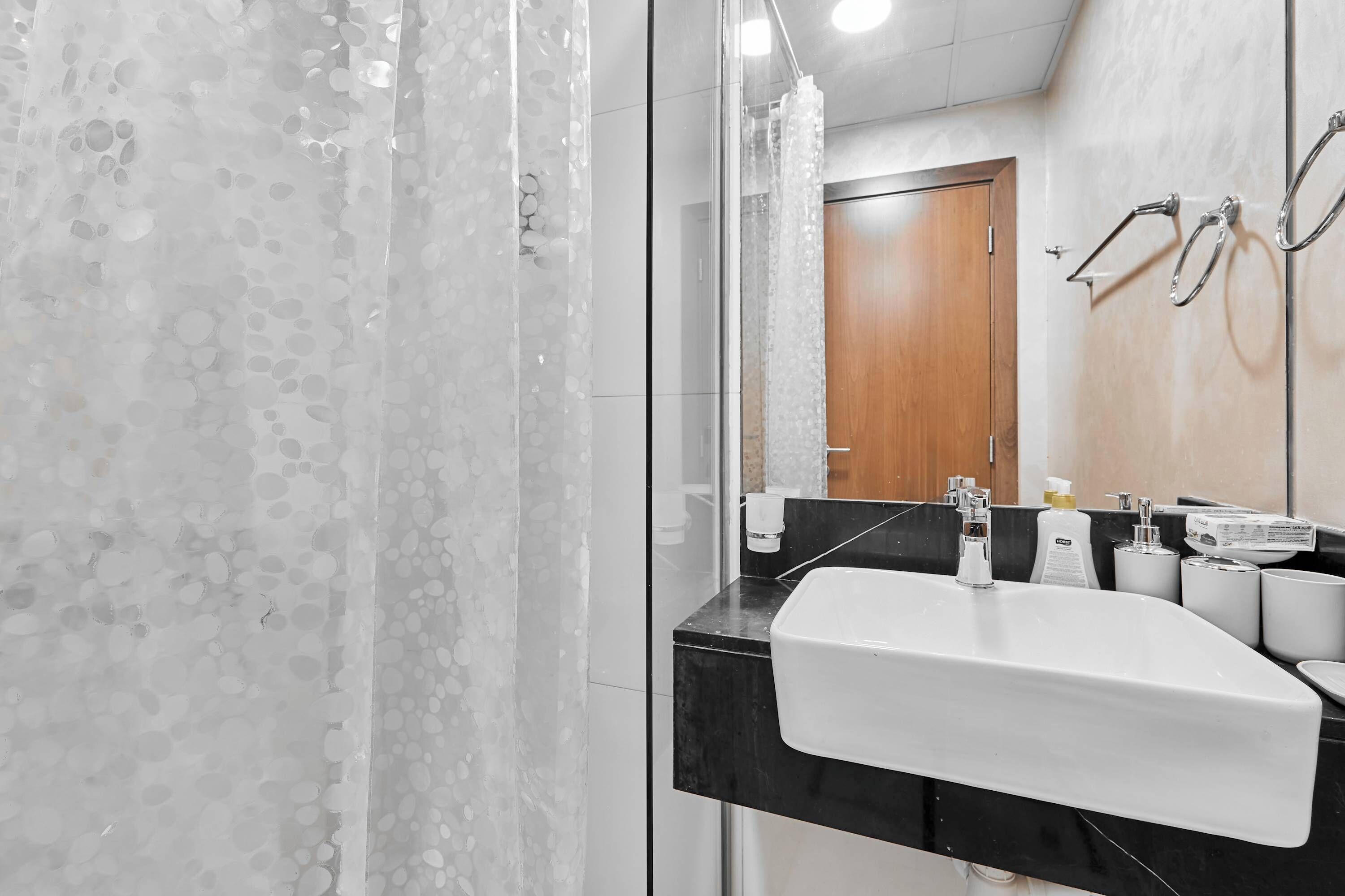 Un baño moderno con lavamanos blanco, encimera negra y cabina de ducha de vidrio.