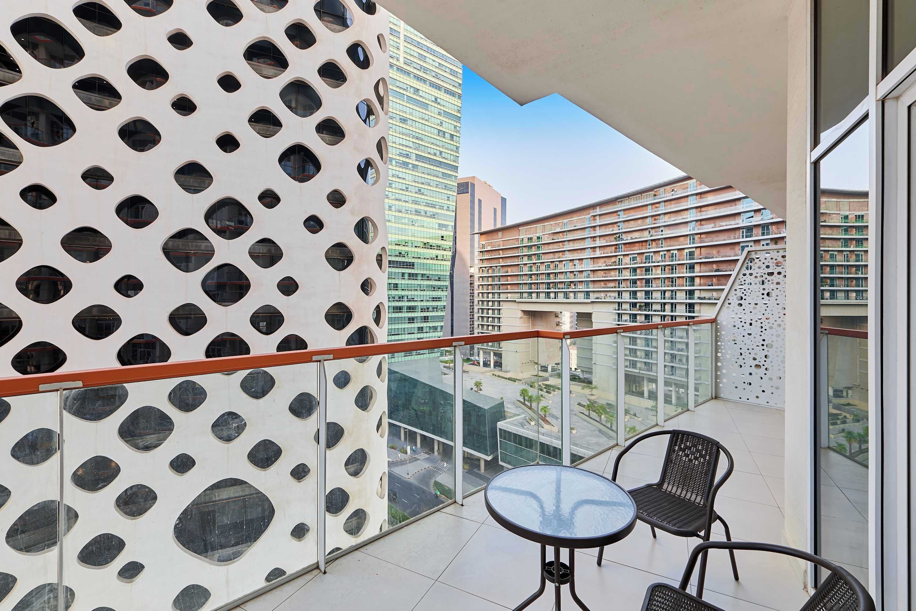 A balcony with a patterned wall, a glass railing, and two chairs.