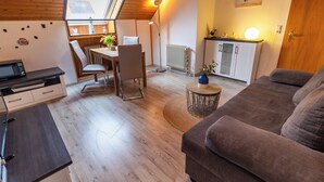 A cozy loft-style living space with a dining area, kitchenette, and a large window providing natural light. - Klara vacation apartment in Greetsiel - quiet and in the middle of it all (Greetsiel)