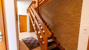 A wooden staircase leading to a room with a brick wall and a white textured wall on the right. - Klara vacation apartment in Greetsiel - quiet and in the middle of it all (Greetsiel)