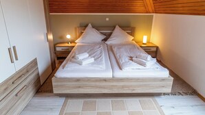 A double bed with white linens and pillows, wooden headboard, bedside lamps, and a wooden ceiling. - Klara vacation apartment in Greetsiel - quiet and in the middle of it all (Greetsiel)
