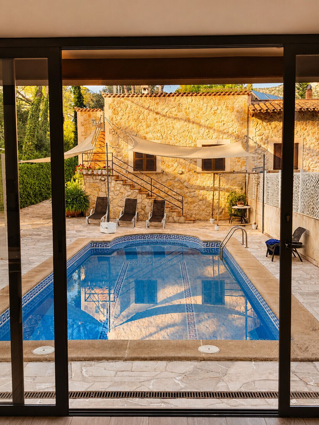 Une piscine avec un mur en pierre et un espace de repos couvert, équipé de chaises.