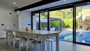 A modern kitchen with a large dining table and chairs, a built-in refrigerator, and a view of a swimming pool and outdoor seating area. - NEW CA NA CARMEN HOUSE with swimming pool (Sa Pobla)