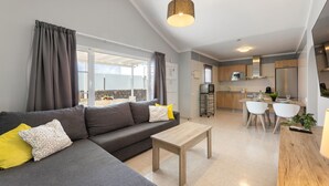 Ein modernes Wohnzimmer mit grauem Sofa, Holztisch und einem Essbereich mit weißen Stühlen.