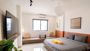 A modern bedroom with a large bed, a flat-screen TV, a window with a view, and a bench by the window. - Mona Hotel (Ho Chi Minh City)