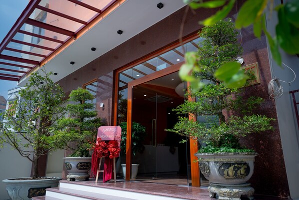 A hotel entrance with a glass door, potted plants, and a sign reading "Grand Momo House". - Mona Hotel (Ho Chi Minh City)