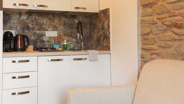 A modern kitchen with white cabinets, a stone backsplash, and a beige sofa in the foreground.