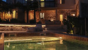 A modern house with a swimming pool, stone walls, and a well-lit exterior at dusk.