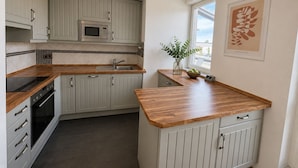 Una cocina con gabinetes grises, un microondas, un fregadero y una ventana con una planta.