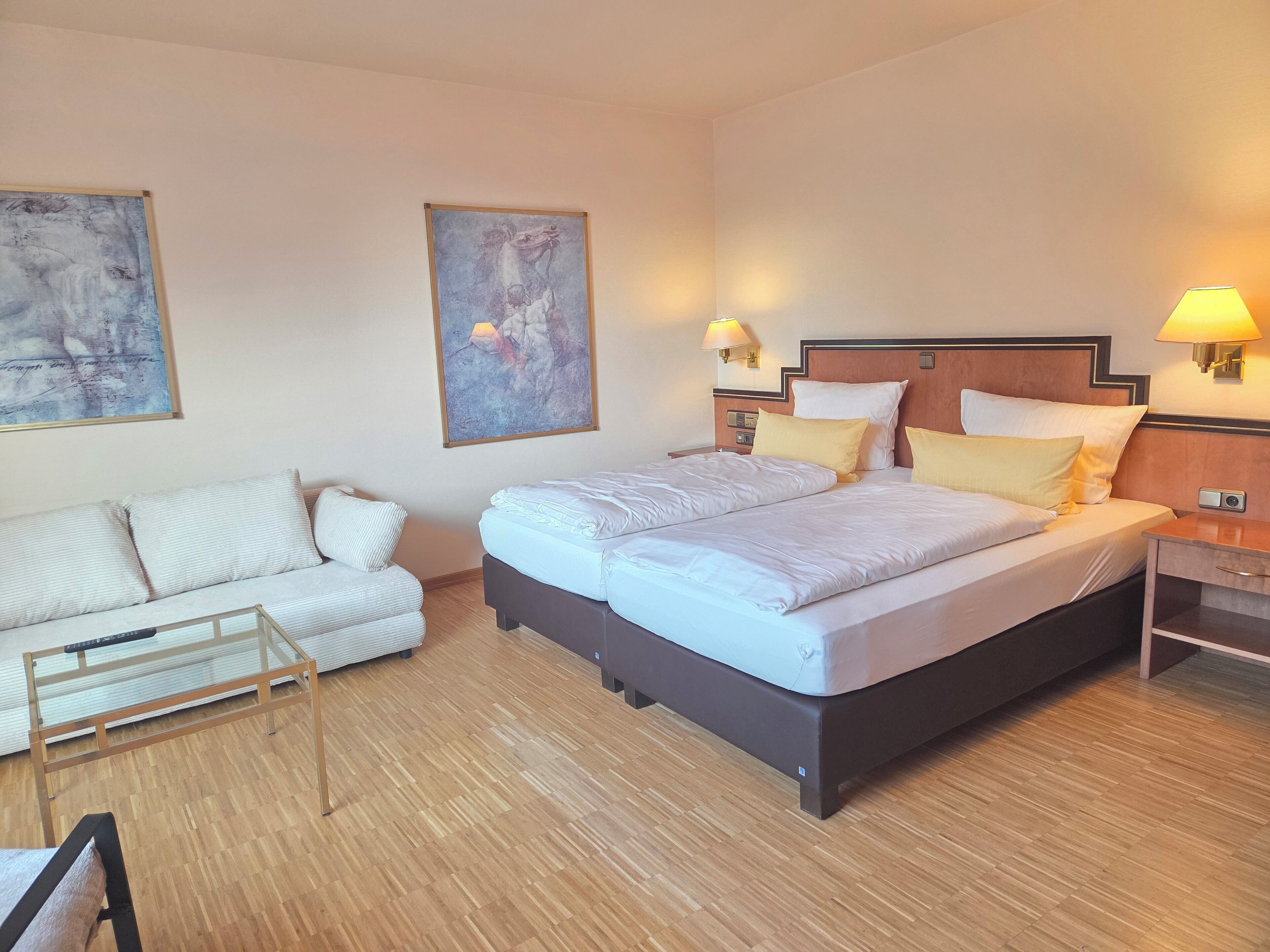 Ein Hotelzimmer mit einem großen Bett, einer Couch, zwei Wandleuchten und abstrakter Kunst an den Wänden.