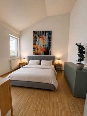 Une chambre à coucher moderne avec un grand lit, une fenêtre, un radiateur, des lampes de chevet et une plante en pot.