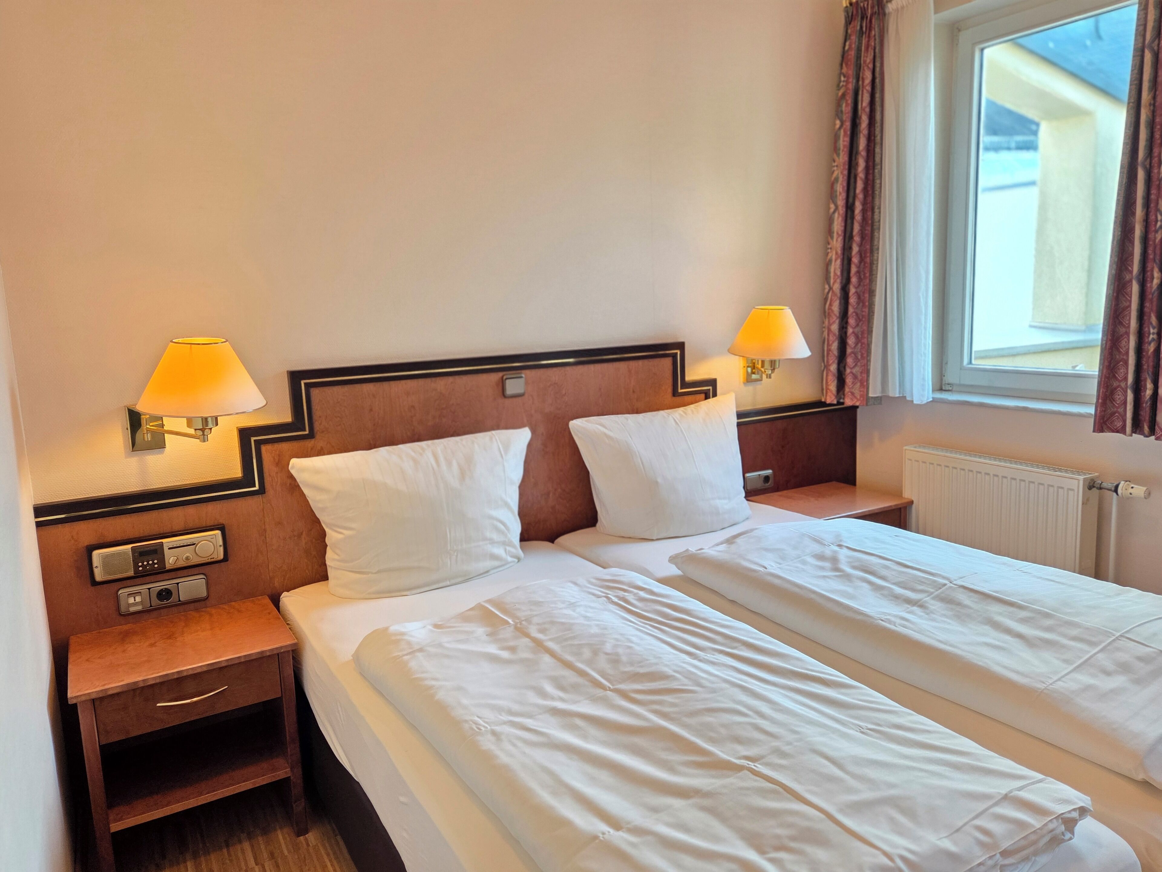 A hotel room with two beds, bedside lamps, a wooden nightstand, and a window with curtains.