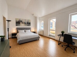 A modern bedroom with a bed, bedside lamps, a desk, and a chair. - Posthaus Aparthotel Residenz (Kronberg)