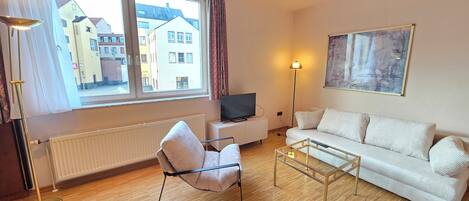 Un salon moderne avec un canapé, un fauteuil et un téléviseur posé sur un meuble.