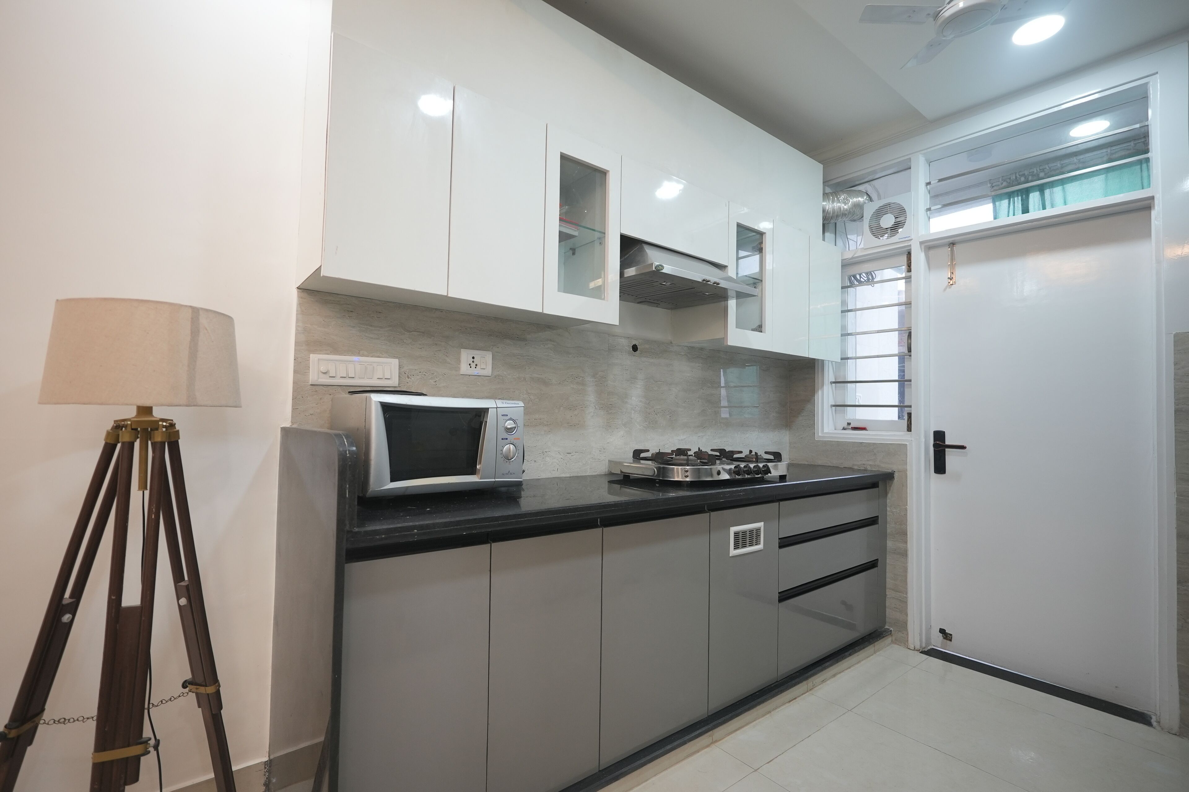 A modern kitchen with white cabinets, a microwave, a gas stove, and a tripod lamp.