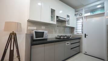 A modern kitchen with white cabinets, a microwave, a gas stove, and a tripod lamp.