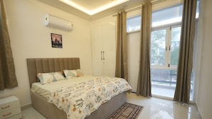 A bedroom with a bed, a wardrobe, an air conditioner, a window with curtains, and a view of the outside.