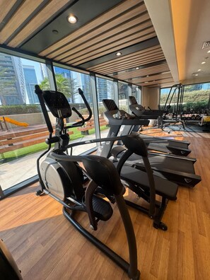A gym with treadmills and exercise equipment, large windows, and a view of a cityscape. - Compact 1BR Apartment (Dubai)