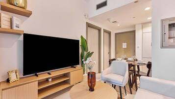 A modern living room with a flat-screen TV, wooden entertainment unit, and a round coffee table with a vase of flowers.