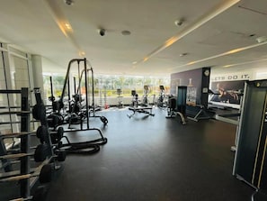 Une salle de sport équipée de divers appareils d’exercice, ornée d’une affiche motivante et dotée de grandes fenêtres laissant entrer la lumière naturelle.