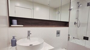 Une salle de bain moderne avec un lavabo blanc, un meuble-lavabo en bois foncé et une cabine de douche en verre.