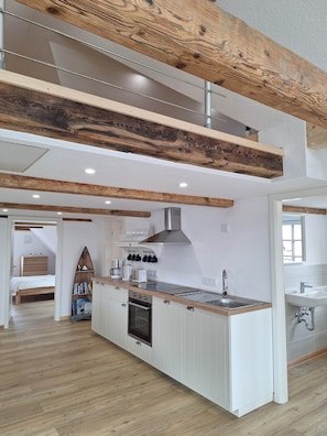 Eine moderne Küche mit einer zentralen Kochinsel, Holzbalken, weißen Schränken und einem eingebauten Backofen.