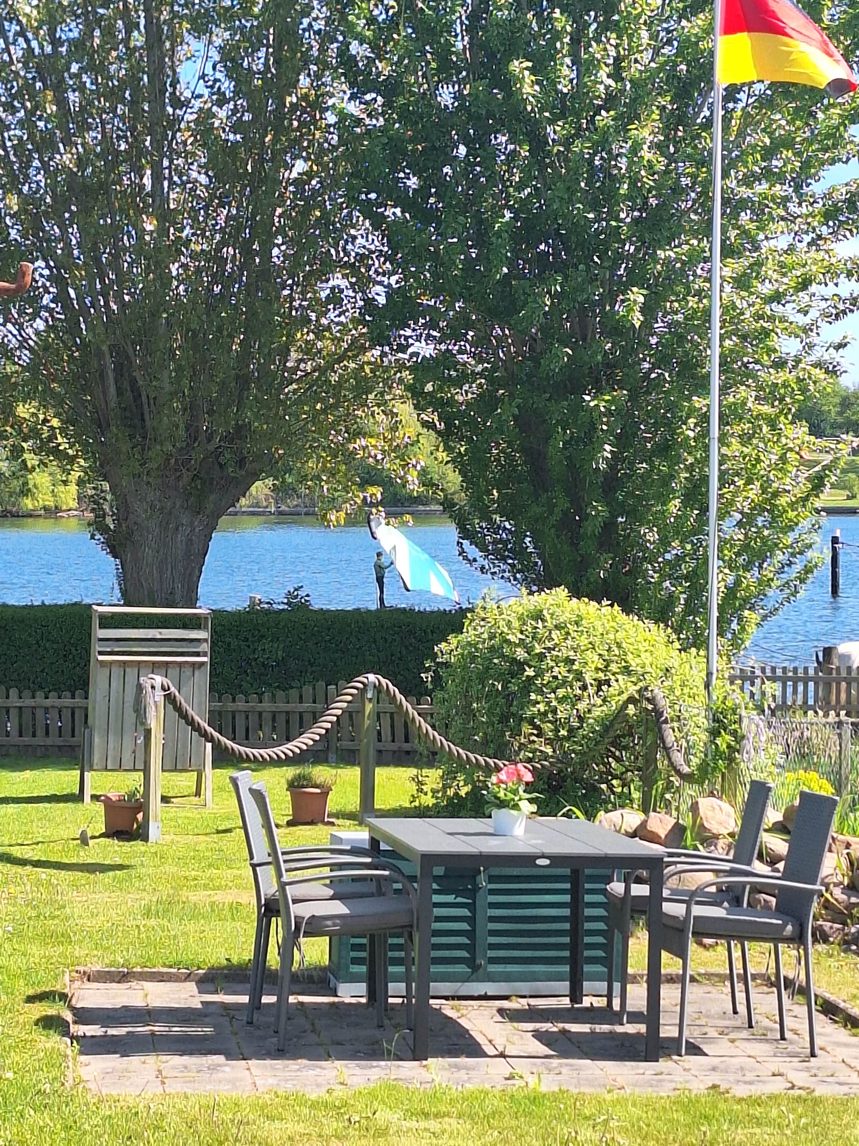 An outdoor seating area with a table and chairs, a flagpole with a flag, and a large tree.