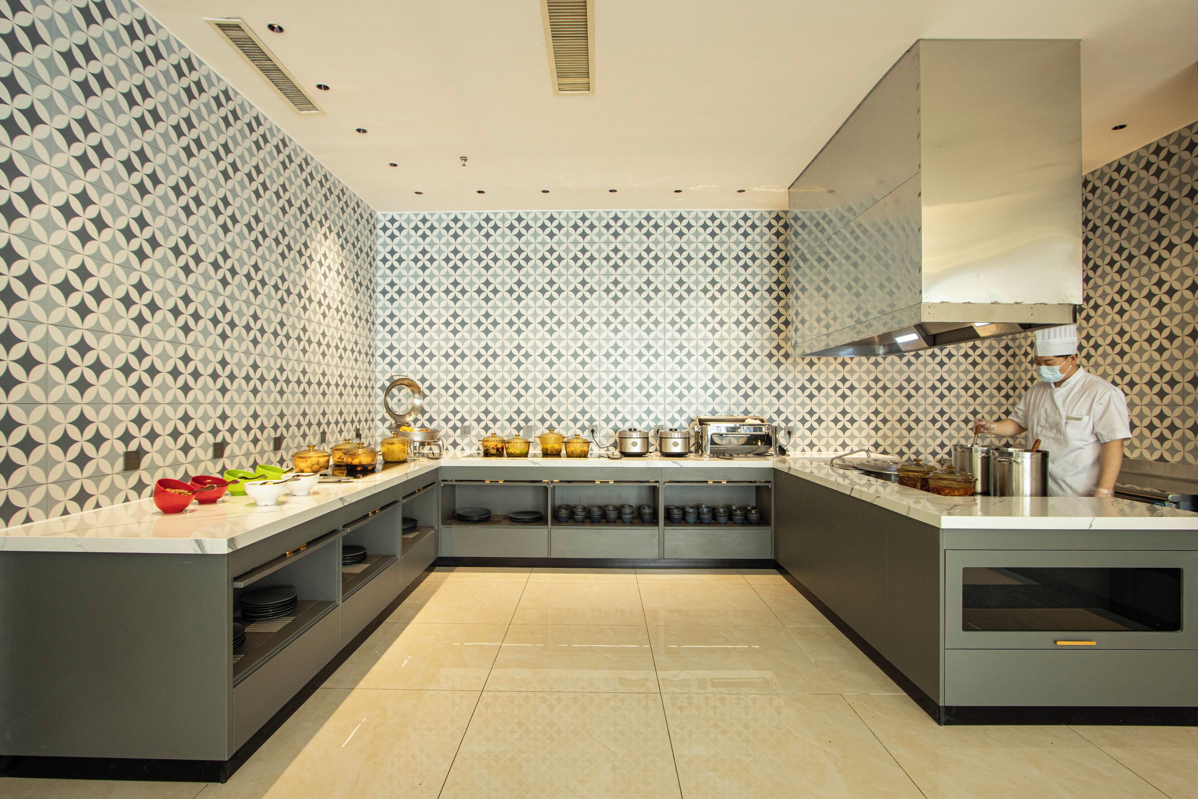 Una cocina moderna con paredes de diseño geométrico, electrodomésticos de acero inoxidable y un chef preparando comida.