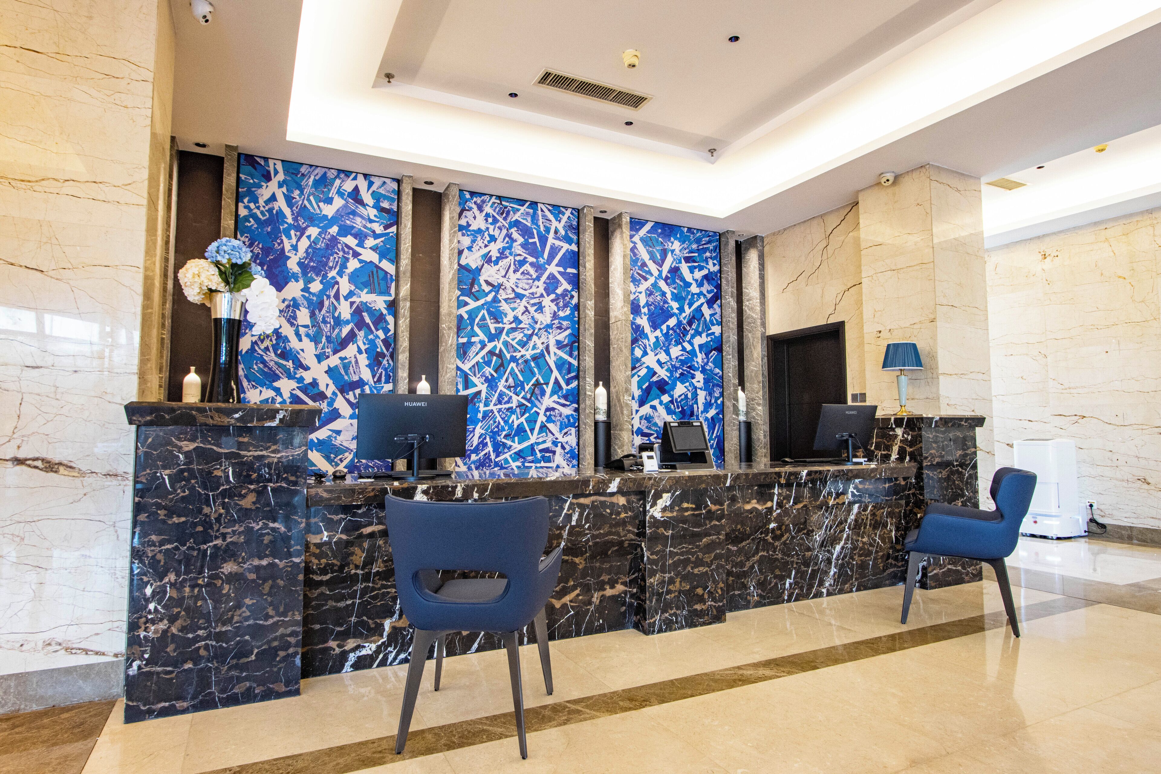 Un espace d’accueil moderne avec des comptoirs en marbre, des chaises bleues et un mur bleu orné d’une œuvre abstraite.