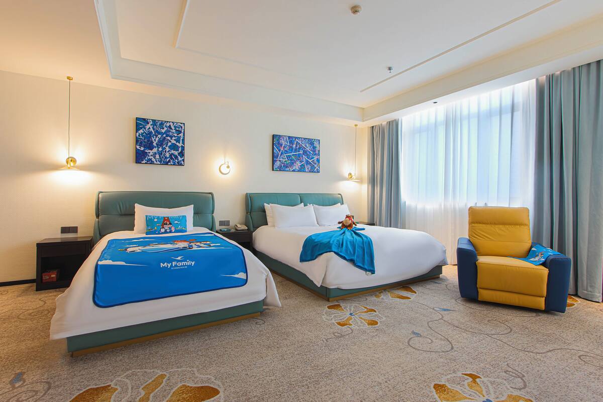 A hotel room with two beds, a chair, and artwork on the walls.