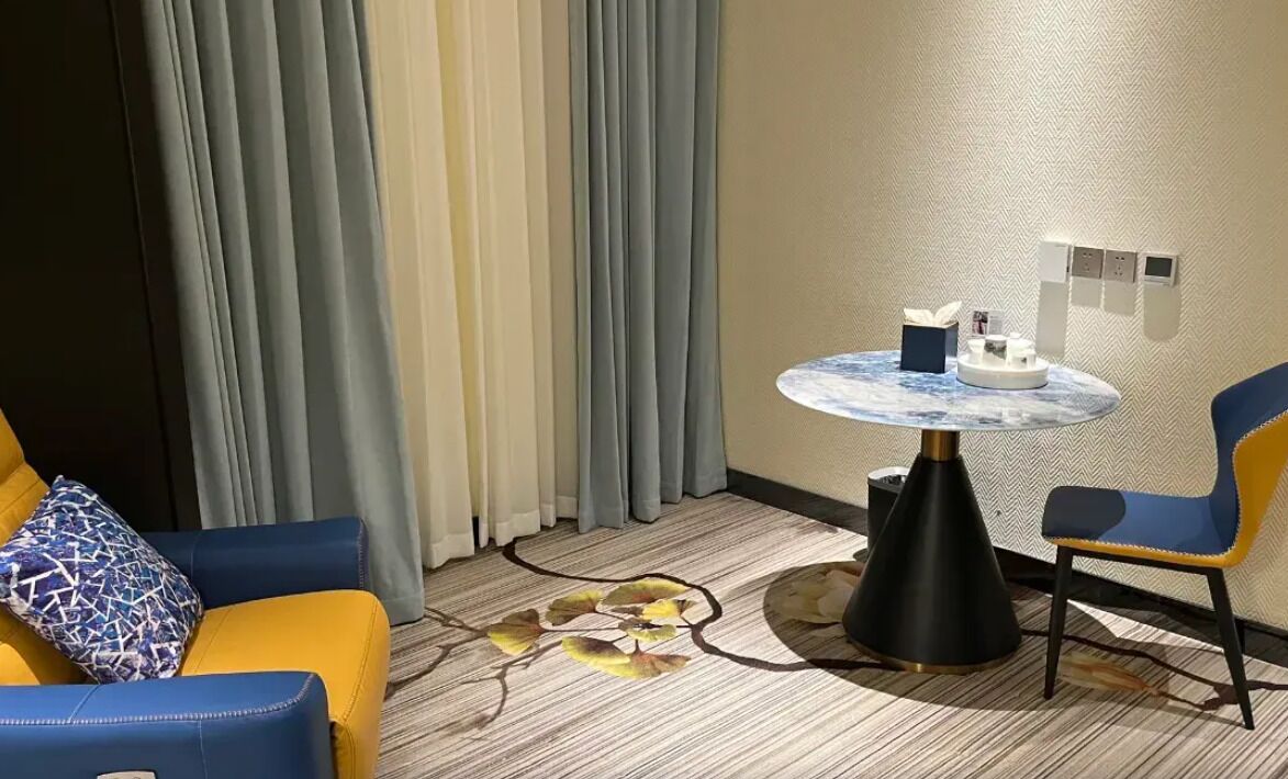 A hotel room with a sofa, a chair, a small round table, and a decorative rug.