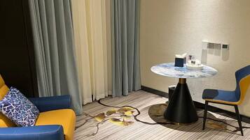 Et hotelværelse med en sofa, en stol, et rundt bord og en dekorativ måtte.