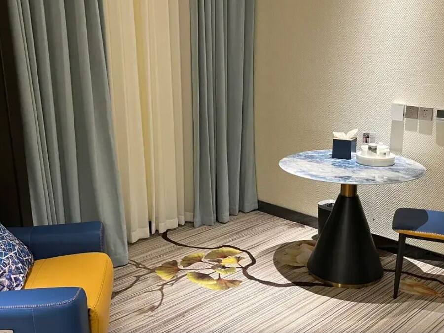 Et hotelværelse med en sofa, en stol, et rundt bord og en dekorativ måtte.