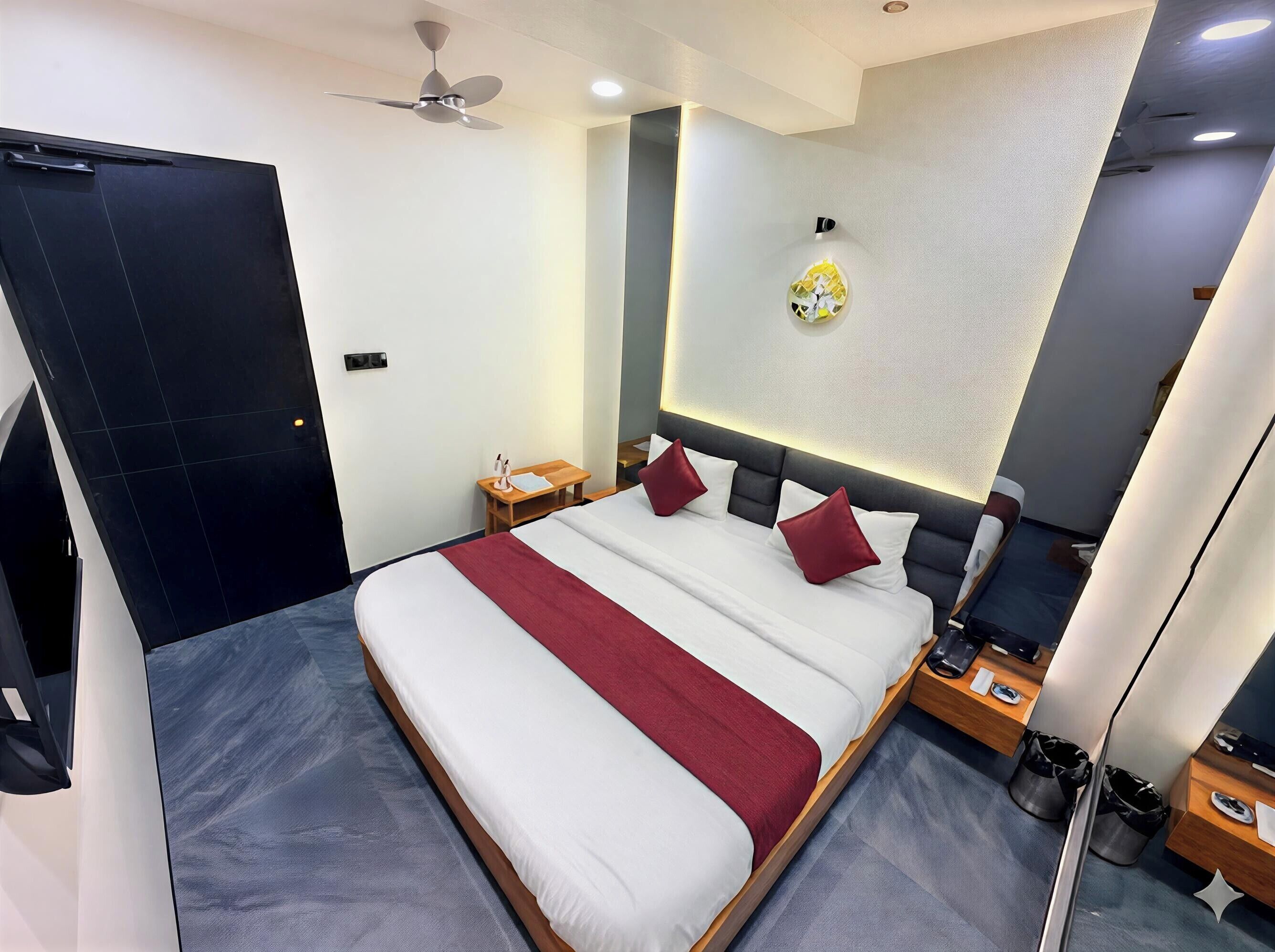 Una habitación de hotel moderna con una cama grande, un ventilador de techo, una mesita de noche con lámpara y un aplique de pared.