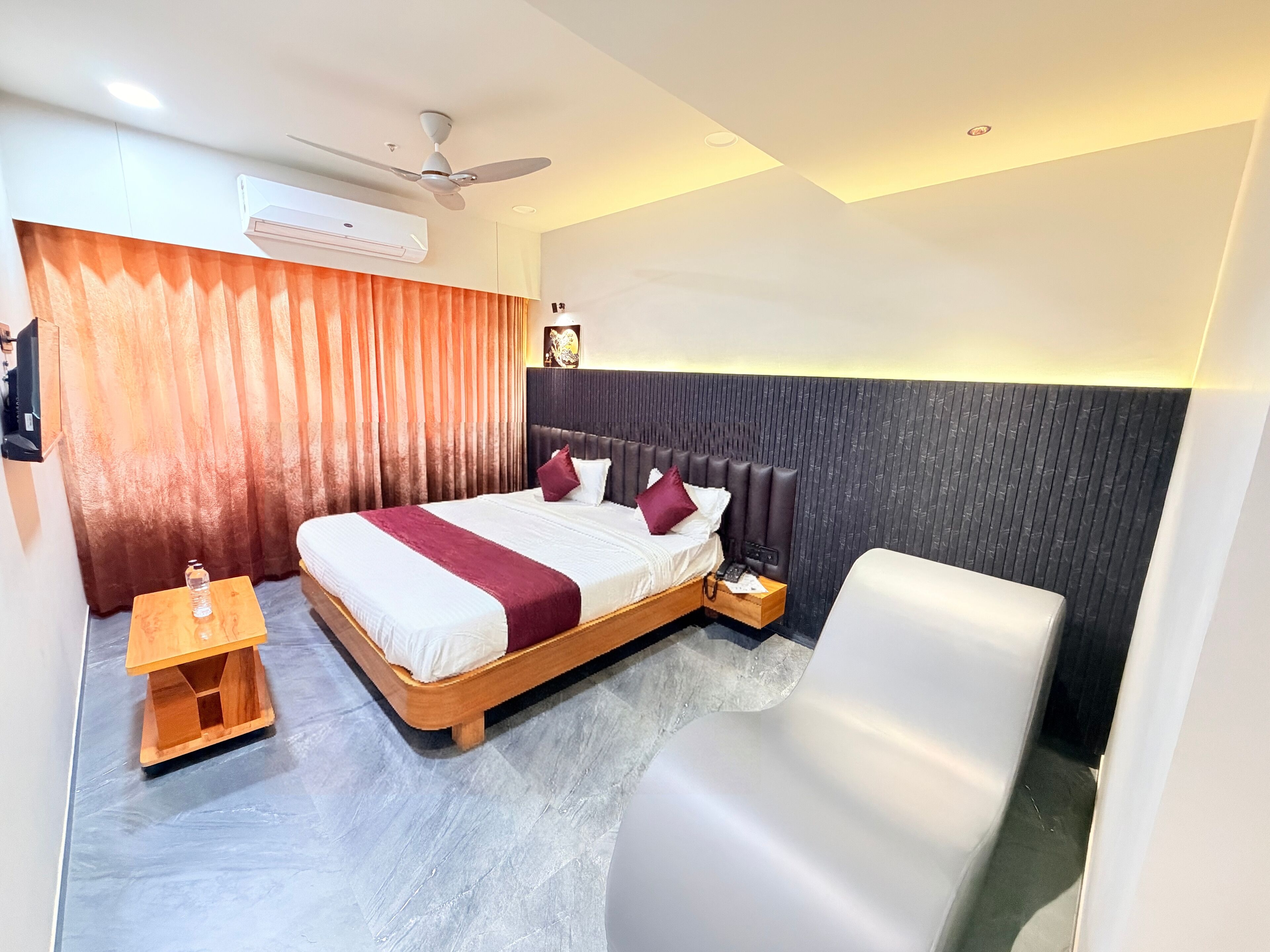 Una habitación de hotel moderna con una cama grande, una mesita de noche, una silla y un ventilador de techo.