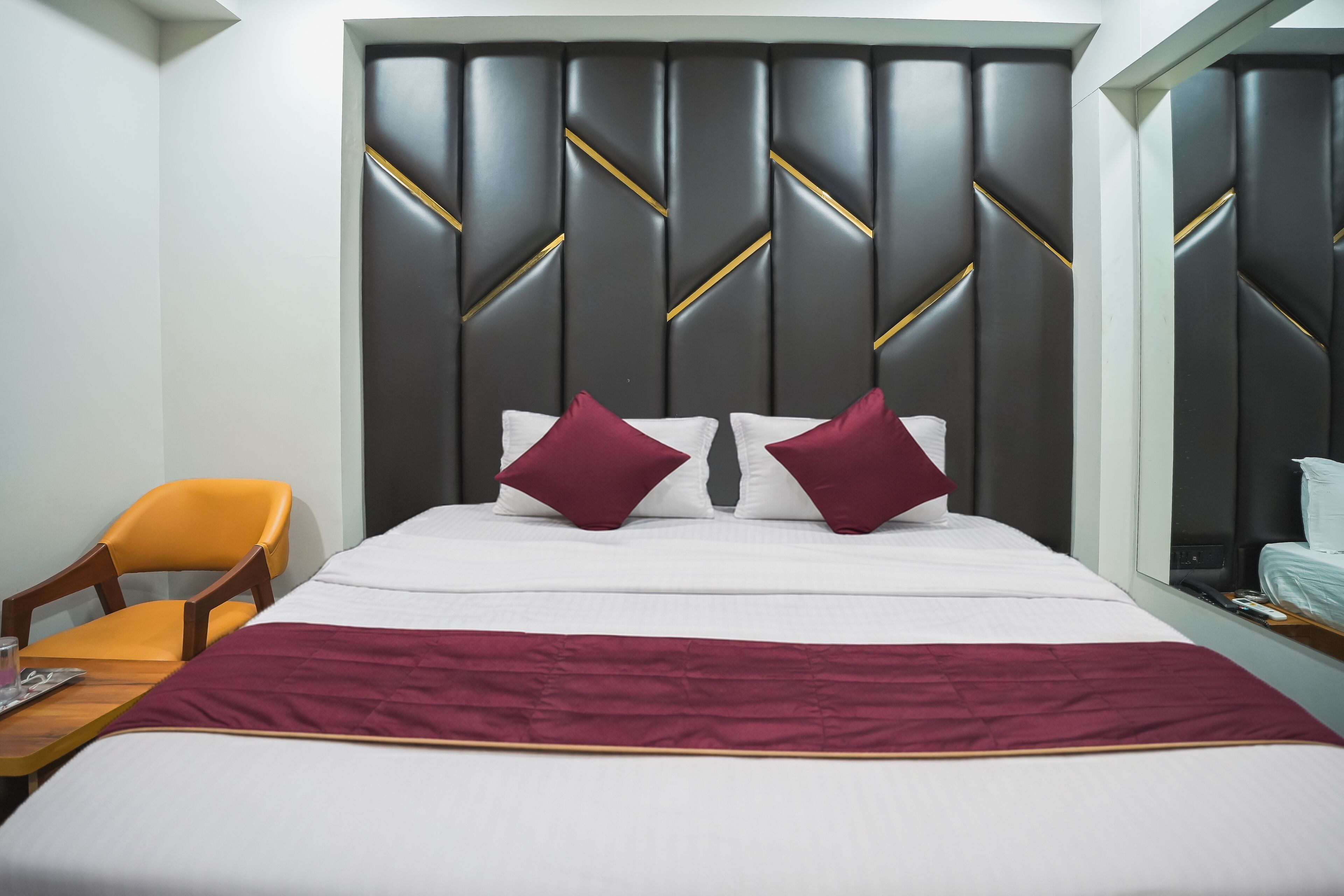 Habitación de hotel con una cama grande, una mesita de noche de madera, una silla y un cabecero con diseño geométrico.