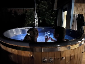 A wooden hot tub with two people inside, surrounded by a wooden deck and a window. - Le Pré Marin (Sotteville-sur-Mer)