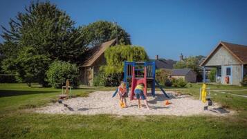 Une aire de jeux avec un toboggan et des structures d’escalade, entourée d’herbe et d’arbres.