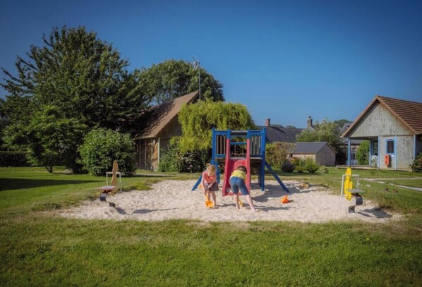 A playground with a slide and climbing structures, surrounded by grass and trees. - Le Pré Marin (Sotteville-sur-Mer)