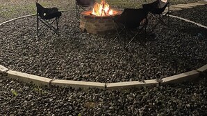 Un hogar con dos sillas, rodeado de piedrecitas, frente a una pared de madera con luces colgantes.