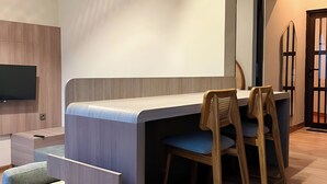 Una habitación moderna con escritorio integrado, dos sillas, televisor y un espejo grande.