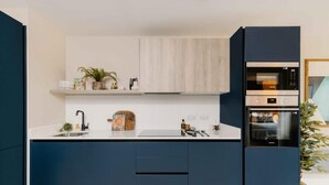 A modern kitchen with a white countertop, dark blue cabinets, and a built-in oven. - City Centre Apartment- Cozy and 5 mins walk to everywhere (Birmingham)