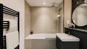A modern bathroom with a bathtub, a large mirror, and a towel rack. - City Centre Apartment- Cozy and 5 mins walk to everywhere (Birmingham)