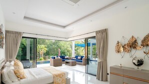 Ein modernes Schlafzimmer mit einem großen Bett, einem Balkon mit Sitzgelegenheit und Blick auf Grünflächen.