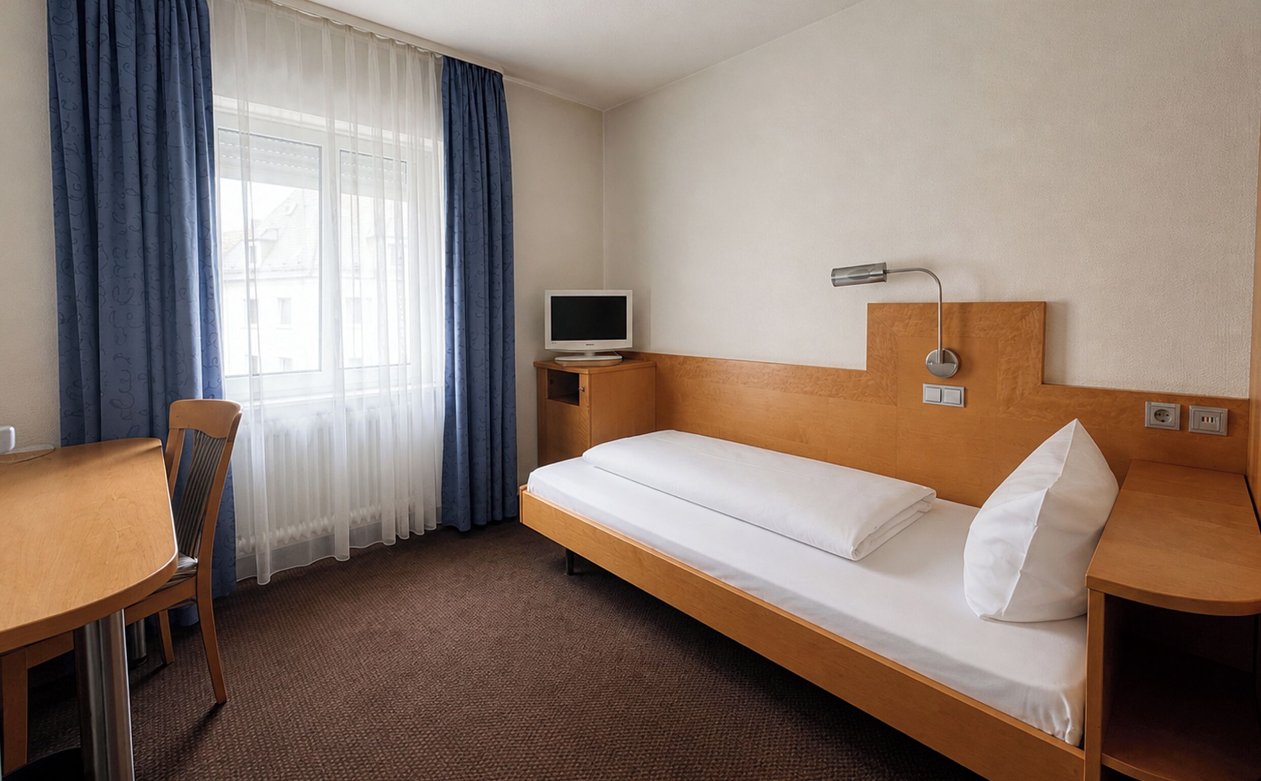 A hotel room with a bed, a desk, a chair, a television, and a window with curtains.