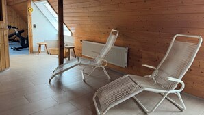 A room with wooden walls, two white wicker lounge chairs, a small table, and a window. - DORMERO Hotel Crailsheim (Crailsheim)