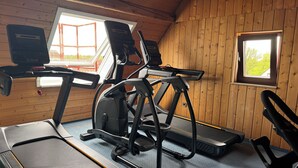 A gym with exercise equipment, including treadmills and an elliptical, in a room with wooden walls and windows. - DORMERO Hotel Crailsheim (Crailsheim)