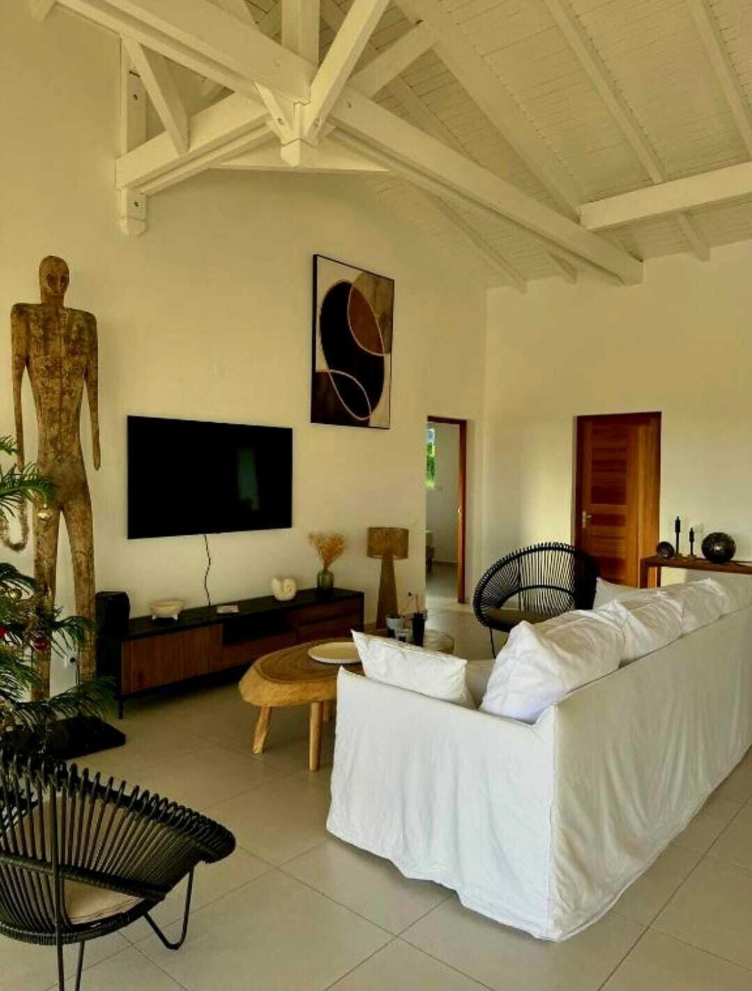A living room with a white sofa, a television, a wooden cabinet, a lamp, and a decorative sculpture.