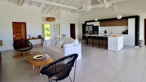 Een ruime woonkamer met een bank, stoelen, een salontafel en een keuken met een bar.