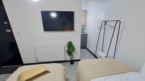 Hotellihuone, jossa on kaksi sänkyä, televisio, patteri, kasvi ja vaateteline.